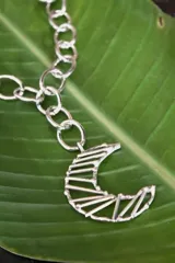 Collar plateado con cadena de eslabones grandes y dije de luna creciente con diseño geométrico calado.