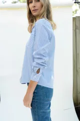 Camisa de popelina a rayas celestes y blancas, de estilo clásico, con cuello camisero, manga larga con puños ajustados, bolsillo frontal aplicado y botones de nácar.