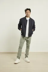 Campera tipo bomber color verde militar, confeccionada en 100% algodón. Cuenta con puños tejidos al tono, cuello y cintura elásticos, y cierre frontal metálico.