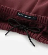 Pantalón de jogging color bordó con paneles laterales en negro y detalles de líneas blancas. Presenta un corte holgado y cintura elástica con cordón de ajuste.