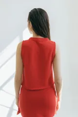 Top tejido en punto arroz color beige, de corte recto y sin mangas, con detalle frontal de lazos finitos decorativos.