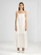 Vestido largo de color celeste confeccionado en tejido arrugado liviano. Presenta un diseño con escote recto, breteles finos y detalles de lazos en los laterales. Incluye bolsillos laterales, forro interno corto y un ruedo asimétrico con caída posterior más larga.