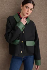 Campera corta de paño negro con cuello, solapas, puños y bolsillos frontales de cuero sintético en color verde. Posee cierre frontal con botones dorados y mangas largas.