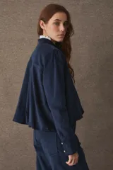 Chaqueta de corte corto y holgado, confeccionada en pana color marrón, con cuello mao, cierre frontal de botones dorados y mangas largas con puños rectos.