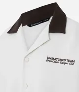 Camisa de manga corta, corte boxy, color crema, con cuello inglés y botones frontales. Presenta un bordado pequeño en el pecho izquierdo con texto en color marrón oscuro.