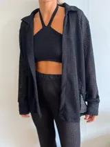 Camisa negra de tejido tipo waffle, de corte holgado y mangas largas. Se usa sobre un top y pantalón haciendo juego.