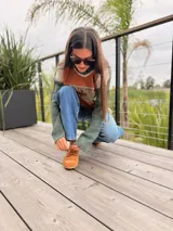 Sweater de diseño artesanal con frente de cuero en color naranja con aplique geométrico, y mangas y espalda tejidas en combinación de colores verde y beige. Presenta cuello en V y corte holgado.