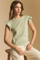 Top tejido sin mangas color negro, con cuello redondo y volados en las sisas con terminación en contraste de punto blanco. Presenta un calce recto y puño inferior acanalado con detalle de punto blanco.