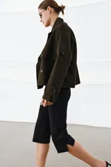 Trench corto de Zara, confeccionado en tejido con algodón con acabado repelente al agua. Presenta cuello solapa, cierre frontal cruzado con botones, mangas largas con trabillas ajustables y bolsillos delanteros.