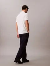 Chomba blanca de piqué de algodón, corte clásico, cuello tradicional, cartera de botones y bajo con aberturas laterales. Tiene un logo bordado en el pecho.