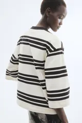 Remera de corte holgado en punto de algodón pesado con diseño a rayas horizontales negras y fondo blanco, cuello redondo acanalado en contraste, hombros caídos y mangas tres cuartos amplias.