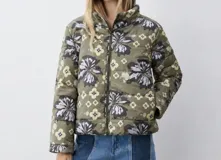Campera puffer color verde militar con estampado floral grande y detalles geométricos, cuello alto y cierre frontal con cremallera.