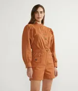Mono corto color ladrillo, de sarga de algodón, con cuello mao, mangas abullonadas largas, cierre frontal con botones dorados, bolsillos laterales y cintura marcada.