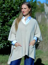 Poncho de lana color beige con escote en V, mangas cortas y bolsillos frontales tipo parche.