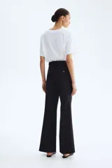 Pantalón negro de corte bootcut, con tiro alto, trabillas para cinturón y cierre frontal con botón y cremallera. Cuenta con pliegues marcados al frente y bolsillos simulados con solapa en la parte delantera.