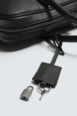 Maletín de cuero negro con acabado abatanado, cierre de cremallera, doble asa de mano, asa de hombro ajustable y extraíble, bolsillo interno para dispositivos electrónicos de hasta 13 pulgadas y detalle de candado. Marca Mango.