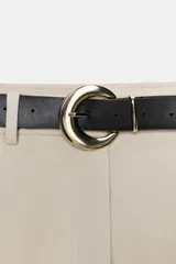 Falda pantalón corta de tiro medio color beige claro, con cierre frontal y detalle de cinturón negro con hebilla metálica redonda dorada.