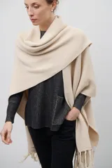 Ruana de tejido de punto en color beige, con diseño envolvente y terminaciones con flecos en el ruedo.