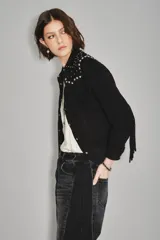 Camisa negra de gamuza caprina con cuello y hombros adornados con tachas metálicas plateadas. Presenta flecos decorativos en el canesú y botones plateados en el frente.