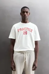 Camiseta de algodón gris melange con cuello redondo, mangas cortas y efecto lavado. Presenta un estampado de texto frontal en color oscuro con efecto desgastado.
