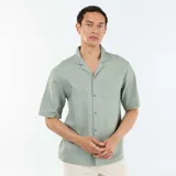Camisa de manga corta color verde claro, de corte holgado, con cuello solapa y bolsillo parche en el pecho.