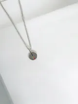 Collar de acero quirúrgico con dije circular calado que representa la flor de la vida, adornado con siete pequeñas piedras de colores que simbolizan los chakras.