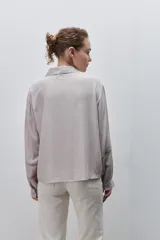 Camisa de viscosa color celeste, de calce amplio y caída fluida, con cuello clásico, cierre frontal de botones y detalles calados en mangas y delantero.