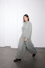 Pantalon de corte amplio tipo balloon, color verde grisáceo, con elástico en la cintura, bolsillos laterales y tiras ajustables en los tobillos para fruncir.