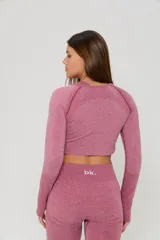 Conjunto deportivo de tres piezas en color rosa viejo, compuesto por un top de bretel ancho, un top de manga larga y una calza chupín. Las prendas presentan un diseño sin costuras con detalles de tejido texturizado y el logo de la marca estampado en blanco.