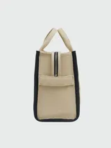 Bolso tipo tote de lona color negro con letras blancas bordadas en el frente que dicen 'THE TOTE BAG MARC JACOBS'. Cuenta con asas superiores cortas y una correa de hombro ajustable y extraíble.
