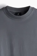 Remera gris de algodón de peso medio, corte oversized, con cuello redondo ribeteado, hombros caídos y bajo recto.