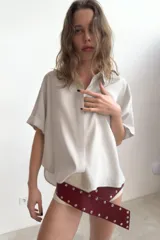 Camisa de corte fluido con cuello solapa y manga corta con dobladillo. Presenta cierre frontal con botones ocultos bajo una tapeta.