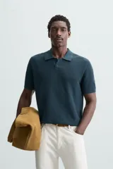 Polo de manga corta color verde azulado oscuro, confeccionado en tejido de punto con textura. Presenta cuello solapa y cierre frontal de botonadura.