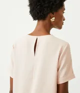 Blusa blanca de poliéster de corte recto, con cuello redondo, mangas cortas con dobladillo y detalles de pespuntes a contratono.