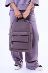 Mochila de diseño minimalista en color lila, confeccionada en material sintético resistente. Cuenta con un compartimento principal amplio, dos bolsillos frontales con cierre y asas superiores reforzadas en color negro.