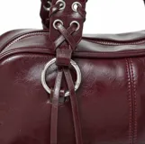 Bolso tipo barrel o doctor bag de cuero charol color vino tinto. Presenta dos asas superiores con detalle de trenzado y ojales metálicos, y múltiples tiras largas de cuero colgando de los herrajes circulares frontales. Incluye correa ajustable para llevar al hombro.