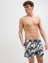 Short de baño con estampado floral abstracto en tonos verdes, beige y blancos sobre base gris oscuro. Presenta cintura elástica con cordón ajustable y bolsillos laterales.