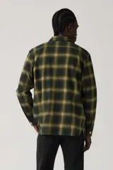 Camisa de manga larga a cuadros en tonos verde oscuro y amarillo, con cuello clásico, cierre de botones frontales y dos bolsillos con solapa en el pecho.