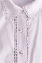 Camisa de algodón color lila, con cuello camisero ribeteado en encaje, cierre frontal de botones con detalles de encaje a los lados y mangas globo largas con puños elásticos.