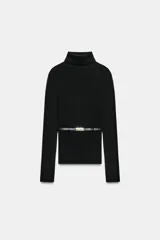 Jersey de punto liso confeccionado en 100% lana, con cuello subido y manga larga. Incluye un cinturón fino integrado a la altura de la cintura con hebilla metálica.