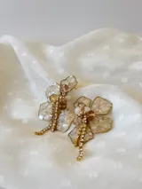 Aros colgantes con forma de flor, pétalos de resina color champagne con borde dorado, centro con cuentas de cristal color ámbar y blanco, y flecos de strass dorados.