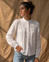 Camisa de broderie blanca con detalles calados, cuello alto con volado, mangas largas con puños y cierre frontal de botones.