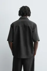 Camisa de manga corta con corte relajado, confeccionada en tejido fluido con mezcla de lyocell. Presenta cuello solapa, cierre frontal con botonadura oculta por solapa y aberturas laterales en el bajo.