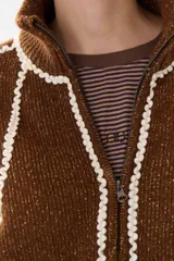 Campera de tejido de punto color marrón con destellos de lurex, corte oversize y cierre frontal. Presenta detalles de costuras y terminaciones en color crema, cuello alto y bolsillos frontales.