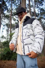 Campera puffer con diseño bicolor, presentando una parte superior en negro y el resto en blanco con estampado tipográfico de la marca. Posee cuello alto, cierre frontal completo y puños elásticos.