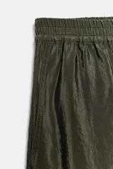 Pantalón de tiro alto color verde militar, confeccionado en tejido satinado con acabado brillante. Presenta cintura elástica fruncida, bolsillos laterales ocultos en las costuras y perneras de corte ancho.