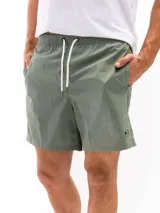 Short de baño de poliéster color verde oliva, con cintura elástica y cordón de ajuste blanco. Presenta bolsillos laterales y un pequeño parche cuadrado negro con un logo blanco en el lateral inferior derecho.