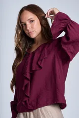 Blusa de color marrón con escote en V, mangas largas abullonadas con puños elásticos y detalles de volados en los hombros y el frente.