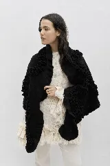 Chal de lana color negro con diseño amplio y envolvente, decorado con volados texturizados que recorren toda la prenda. Confeccionado en tejido de lambswool italiano, ofrece una caída suave y versátil para usar de múltiples formas.