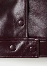 Chaqueta corta efecto piel color bordó, con cuello de solapa y detalle de pelo sintético en el cuello, cierre frontal de botones, bolsillos laterales y forro interior.